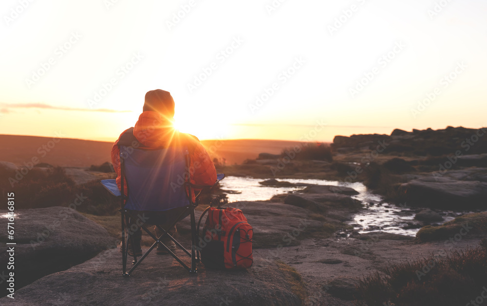 Fototapeta premium mature man hiking in mountain to take timelaps of sunrise, exercise and fitness for wellness, healthy lifestyle and smile. senior mature gentleman sitting on rock, enjoing calm day toned image