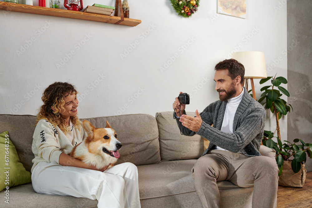 man smiling and taking photo of wife with corgi dog on camera in modern apartment, happy moments man smiling and taking photo of wife with corgi dog on camera in modern apartment, happy moments