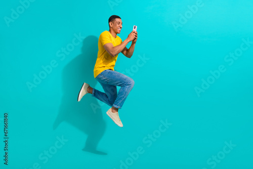 Full length profile portrait of excited handsome guy jump rush use smart phone empty space isolated on turquoise color background