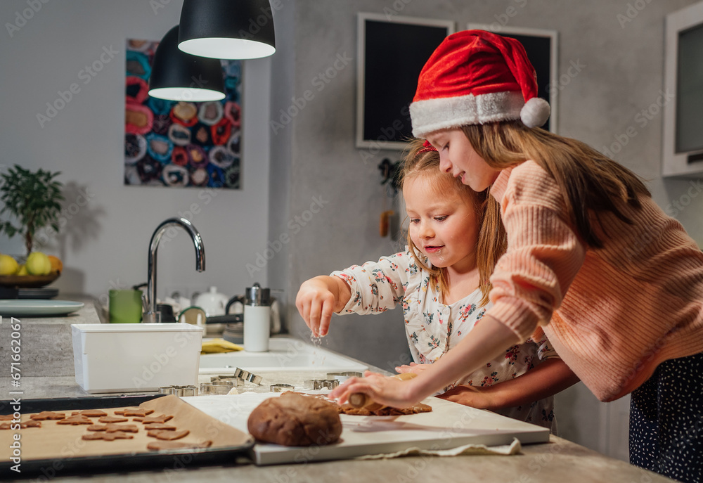 Laughing little girls in red Santa hat kneading Christmas gingerbread dough together on home kitchen tabletop. Happy holiday preparation and childhood concept.. Laughing little girls in red Santa hat kneading Christmas gingerbread dough together on home kitchen tabletop. Happy holiday preparation and childhood concept..