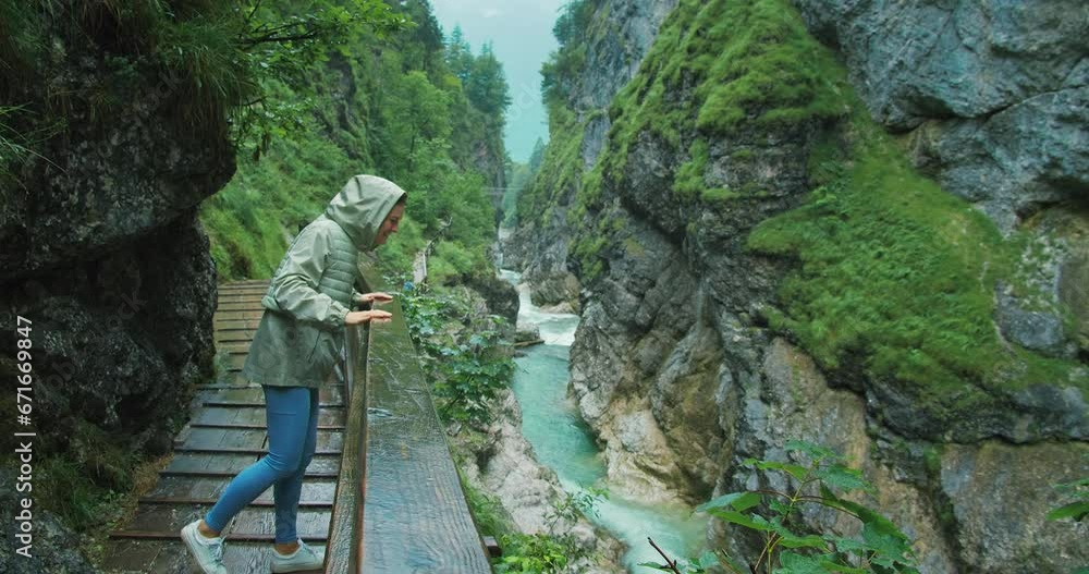 Woman enjoys the rain while hiking in a rocky gorge with mountain fast flowing river. Narrow wooden staircase along the canyon in Austria. Woman enjoys the rain while hiking in a rocky gorge with mountain fast flowing river. Narrow wooden staircase along the canyon in Austria.