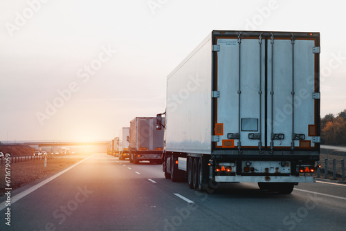 Modern white semi-trailer trucks on the highway driving in the right lane. Commercial vehicle for shipping and post delivery. Shipping of the goods on land with a door-to-door delivery process.