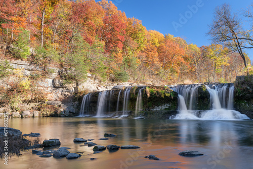 Fototapeta Naklejka Na Ścianę i Meble -  Large waterfall in autumn taken with a long exposure. Cataract Falls in Indiana. Colorful trees in the background that are blurred from the wind. Nice reflections in the river below the falls