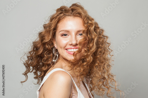Cheerful happy woman with long natural healthy brown curly hair and cute smile looking at camera on white background. Hair care, hair treatment, wellness, joy and cosmetology concept