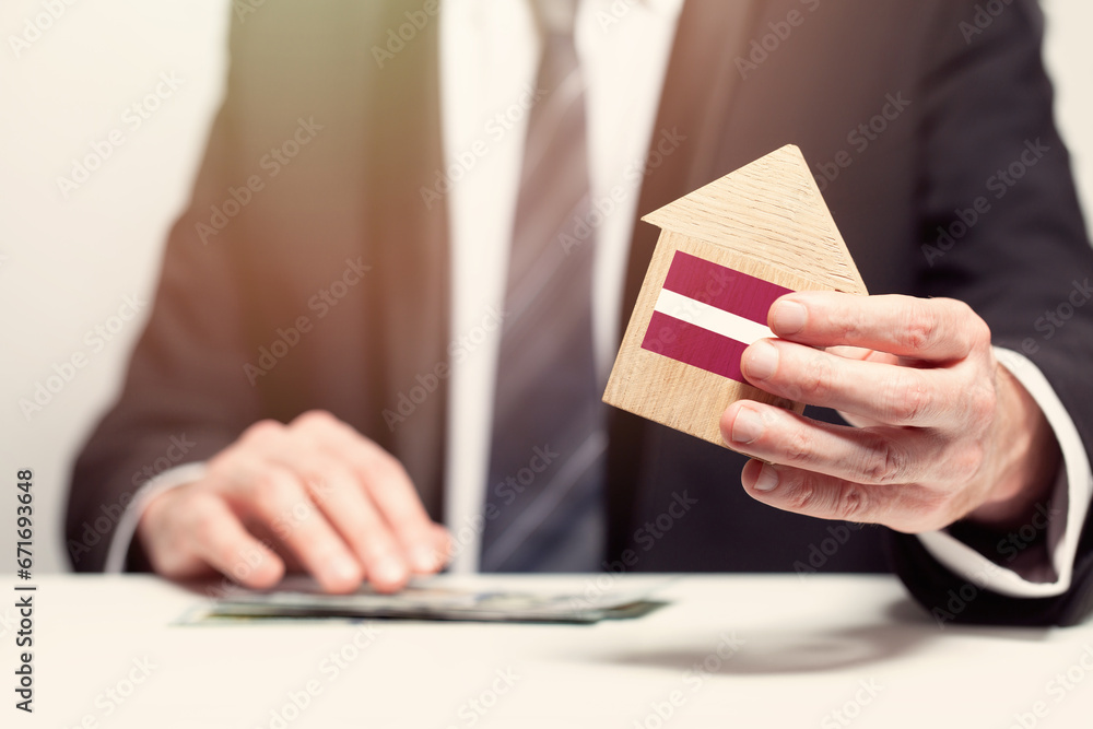 Businessman hand holding wooden home model with Latvian flag. insurance and property concepts Businessman hand holding wooden home model with Latvian flag. insurance and property concepts