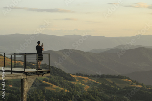 A man stands on a lookout and takes a photo of the mountain landscape with his smartphone © Branimir