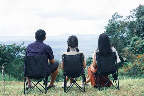 Parents and daughter sit on lawn chairs with look at mountain range and beautiful natural scenery.Back view of a family traveling on holiday
