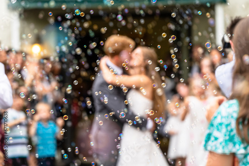 A couple kisses during their wedding exit, as seen through a sea of bubbles