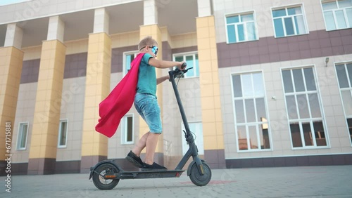 boy superhero on electric scooter. happy family kid dream concept. a lifestyle boy on electric scooter rides on a large square in the city center under a blue sky with clouds sun. superhero boy