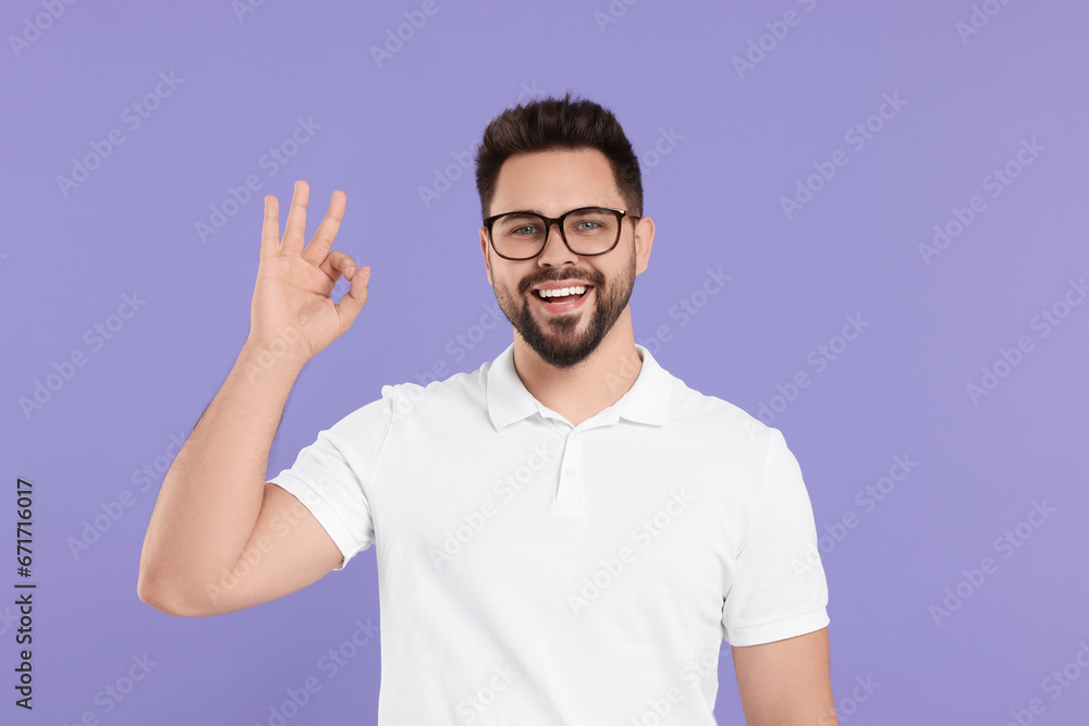 Handsome man in glasses showing OK gesture on violet background Handsome man in glasses showing OK gesture on violet background