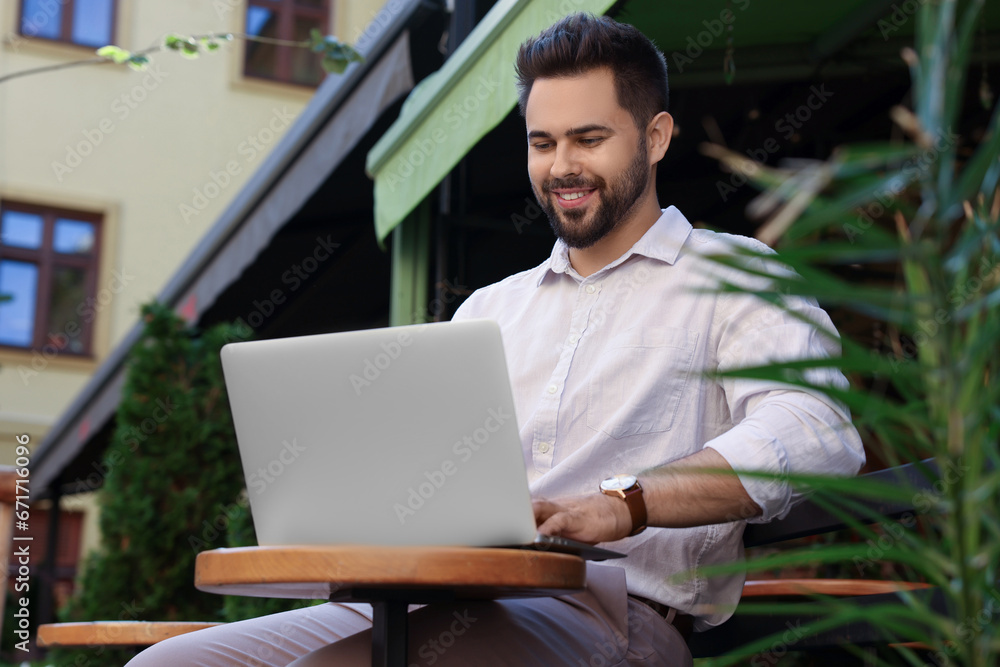 Handsome young man working on laptop at table in outdoor cafe Handsome young man working on laptop at table in outdoor cafe