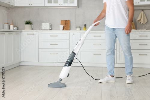 Man cleaning floor with steam mop in kitchen at home, closeup