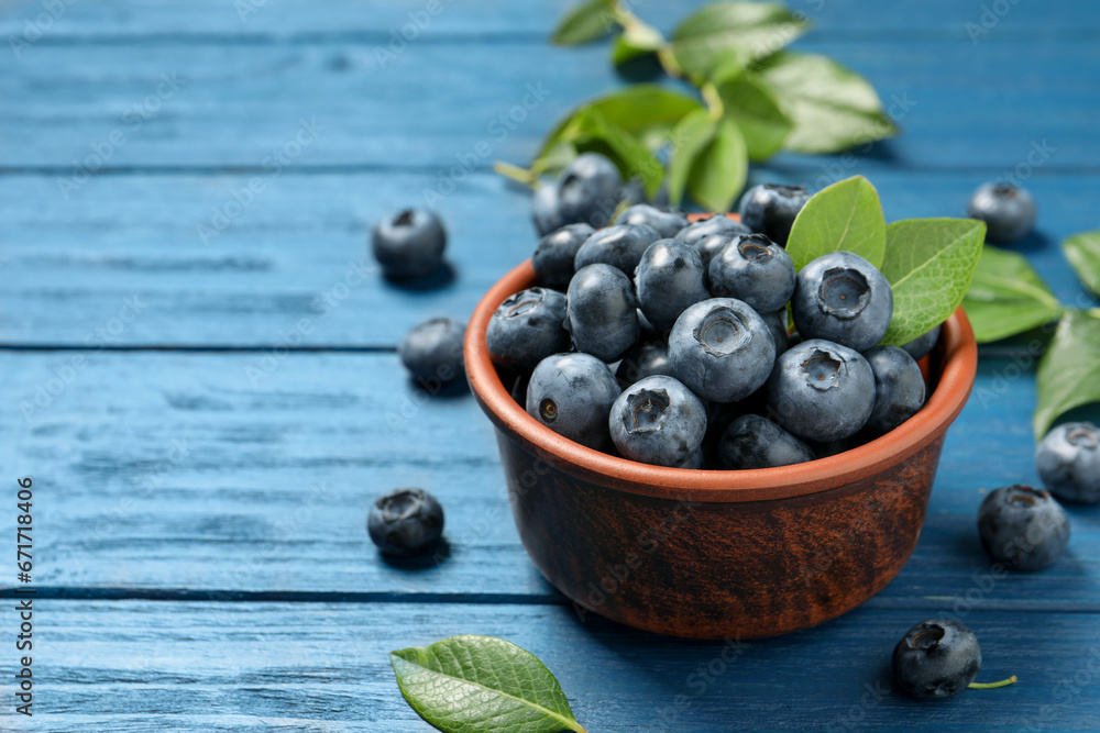 Tasty fresh blueberries with leaves in bowl on blue wooden table. Space for text Tasty fresh blueberries with leaves in bowl on blue wooden table. Space for text