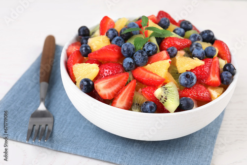 Delicious fresh fruit salad in bowl served on white table, closeup