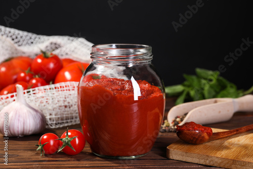 Jar of tasty tomato paste and ingredients on wooden table
