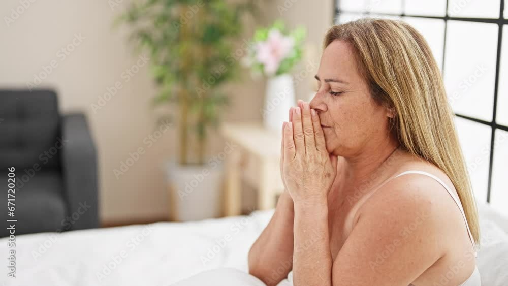 Middle age hispanic woman wearing lingerie sitting on bed praying at bedroom Middle age hispanic woman wearing lingerie sitting on bed praying at bedroom