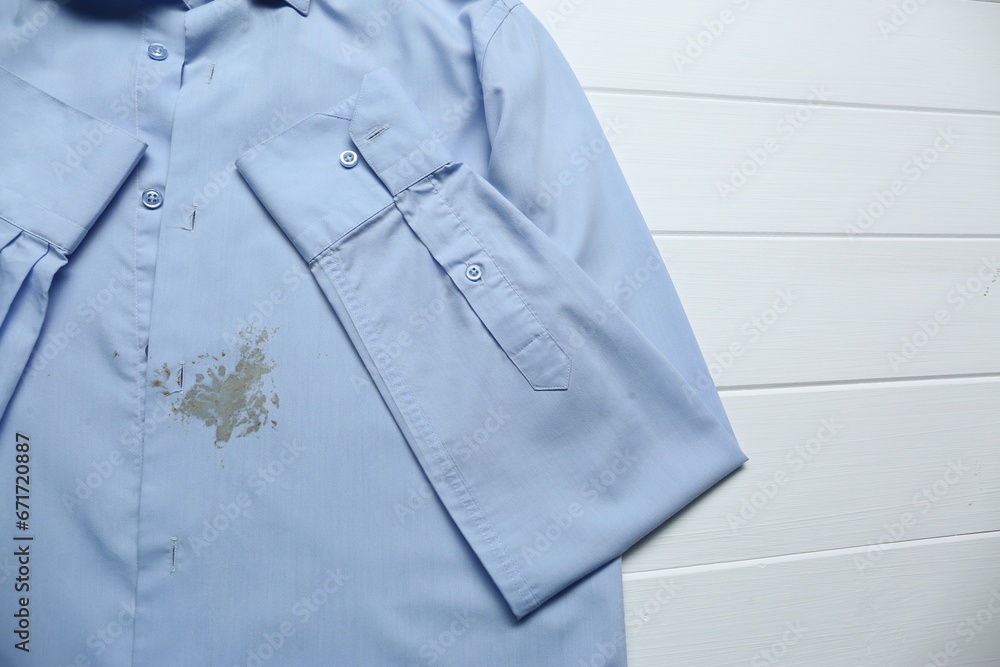 Light blue shirt with stain on white wooden table, above view. Space for text Light blue shirt with stain on white wooden table, above view. Space for text