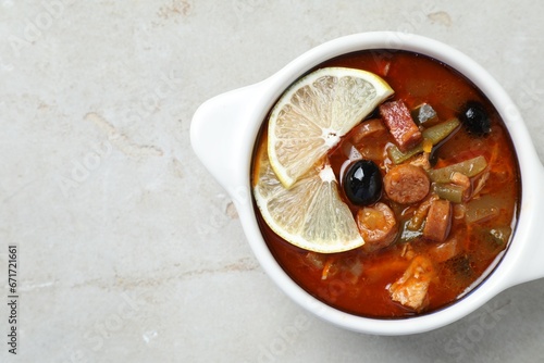 Meat solyanka soup with sausages, olives and vegetables in bowl on white textured table, top view. Space for text