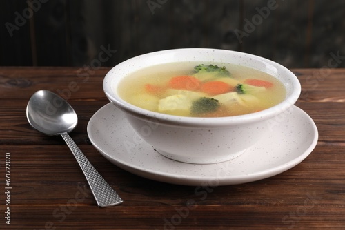 Tasty chicken soup with vegetables in bowl served on wooden table, closeup