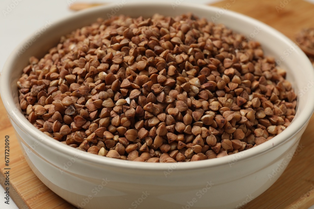 Bowl with dry buckwheat on wooden board, closeup Bowl with dry buckwheat on wooden board, closeup