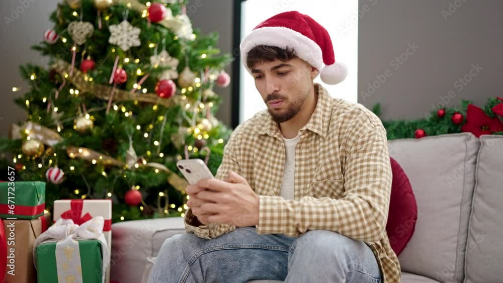 Young arab man using smartphone sitting by christmas tree looking upset at home Young arab man using smartphone sitting by christmas tree looking upset at home