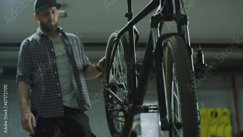 Mechanic turning wheel of bicycle hanging on workstand, then fixing it with screwdriver in repair shop photo