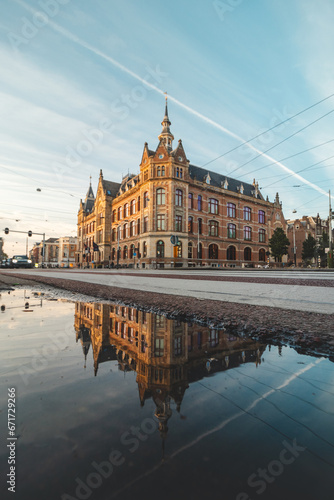 Historic building in the centre of Amsterdam under the light from the sunset at a busy intersection in the middle of the city with a reflection in a puddle