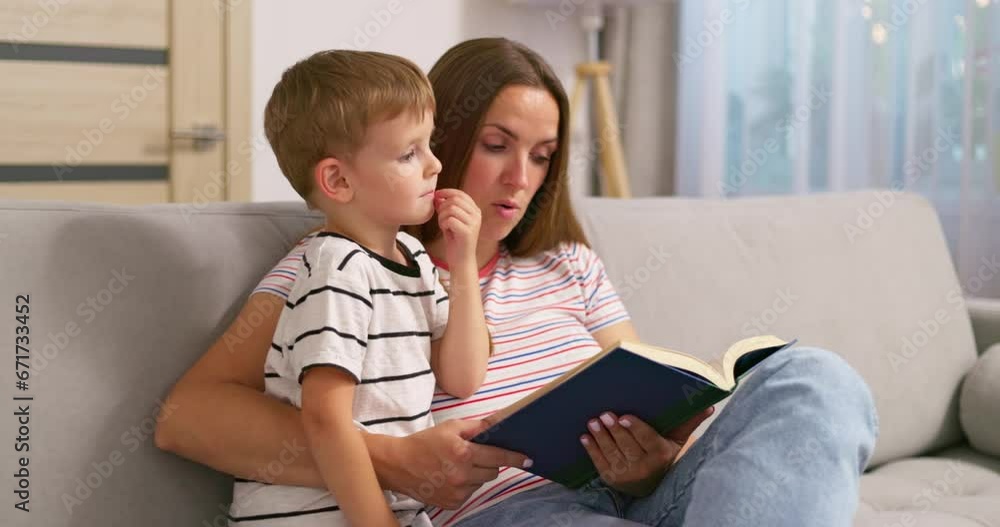 Mother and son are reading a book sitting on a cozy sofa in the living room