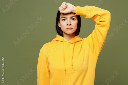 Young sad sick ill bored tired Latin woman wearing yellow hoody casual clothes put hand on forehead suffer from headache isolated on plain pastel green background studio portrait. Lifestyle concept. © ViDi Studio