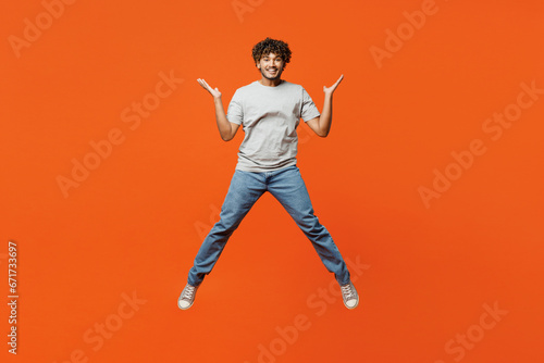 Full body young overjoyed excited smiling happy Indian man he wears t-shirt casual clothes jump high spread hands look camera isolated on orange red color background studio portrait Lifestyle concept