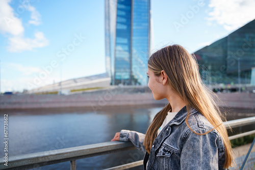 A teenage girl walks next to a high business tower in St. Petersburg photo