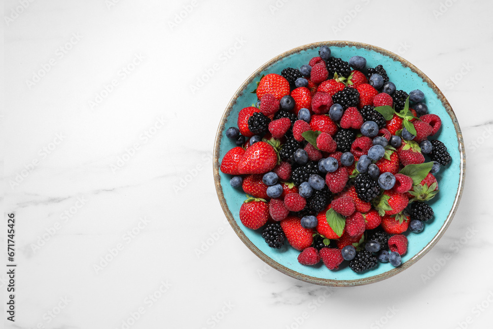 Many different fresh ripe berries in bowl on white table, top view. Space for text Many different fresh ripe berries in bowl on white table, top view. Space for text