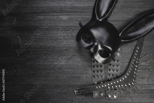 Black rabbit mask, studded leather bracelets and neck choker on the black wooden table background with copy space.