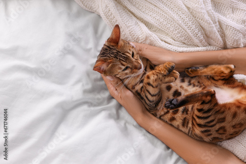 Woman with cute Bengal cat on bed at home, above view and space for text. Adorable pet