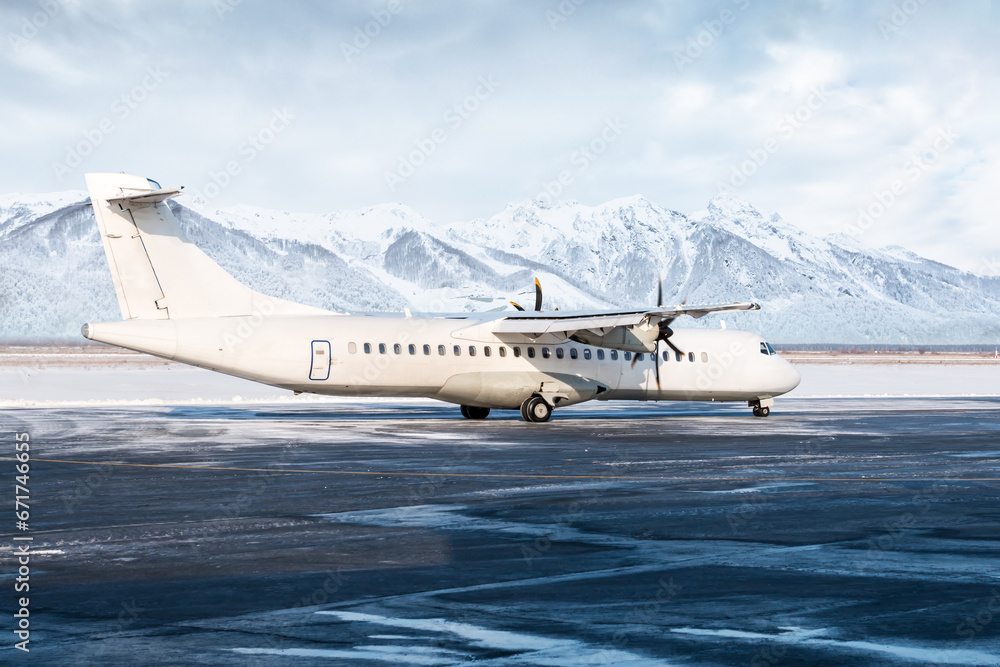 White passenger turboprop airliner on the winter airport apron on the background of high picturesque mountains White passenger turboprop airliner on the winter airport apron on the background of high picturesque mountains