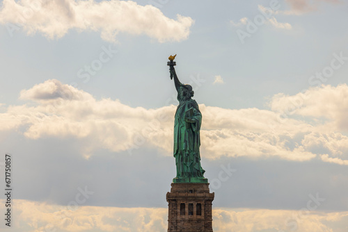An iconic view of Statue of Liberty on Liberty Island in New York set against brilliant blue sky with fluffy white clouds. USA.