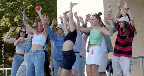 Girl with phone and music speaker in hand shows dance moves to group of young people, peers repeat after her. Social Gathering Friends free time together, entertainment with digital detox. Lifestyle