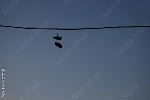 black silhouette of sneakers, Shoes hanging from a telephone wire on blue sky background. Old sneakers hang on an electric wire on a summer day. photo