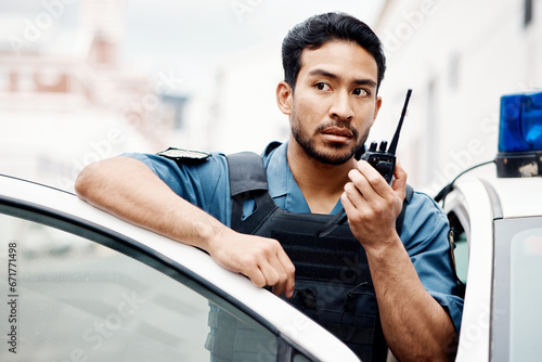 Asian man, police and walkie talkie for radio in city communication, reinforcement or emergency. Serious male person or security guard by cop car and calling backup for crime on patrol in urban town photo