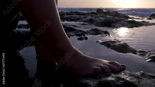 Traveling of bare feet of a woman sitting on some rocks in the sea at sunset