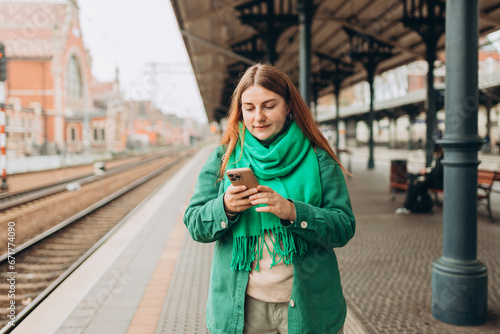 A young and beautiful woman with backpack waiting for a train while using a mobile phone. Passenger using cellphone monitoring traffic schedule via application © mdyn