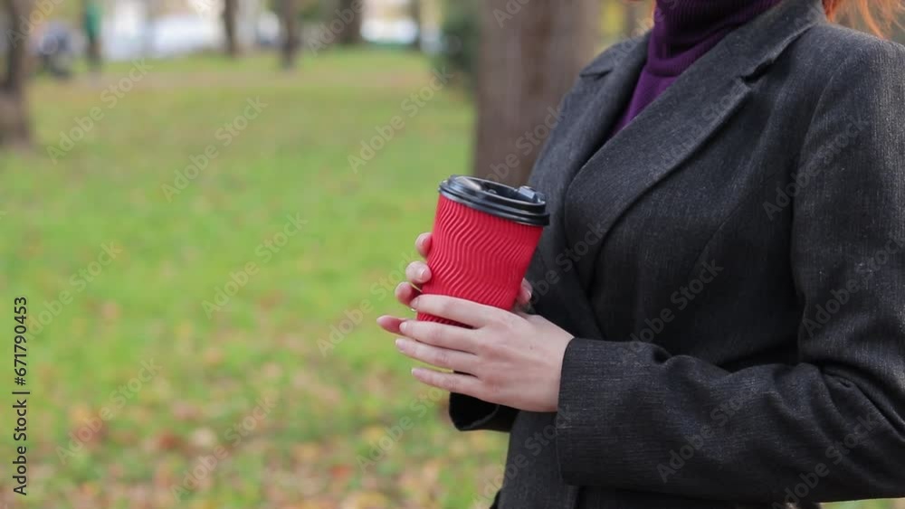 A girl drinks coffee or tea in the park in autumn. Hands with a paper cup close-up. Drink warm drinks in cold weather. Female hands with a cup of coffee A girl drinks coffee or tea in the park in autumn. Hands with a paper cup close-up. Drink warm drinks in cold weather. Female hands with a cup of coffee