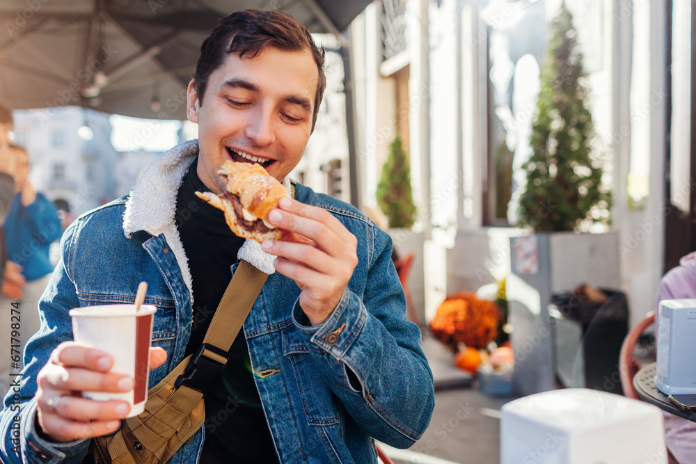 Young happy man having breakfast with coffee and croissant sitting at outdoor cafe in European city. Young happy man having breakfast with coffee and croissant sitting at outdoor cafe in European city.