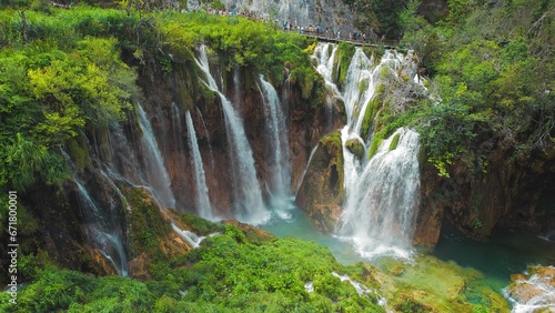 Tourists visit famous Plitvice waterfalls in Croatia. Mountain streams flow into a lake with azure clear water. Summer National Park.