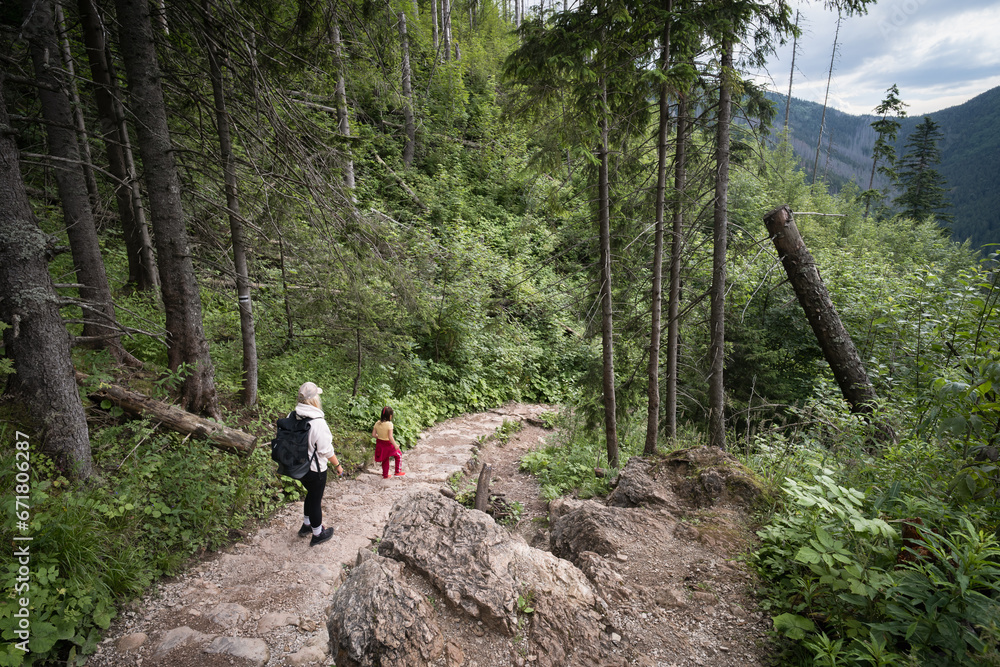 Mom and daughter go hiking in the Polish Tatras along a hiking trail through the forest.