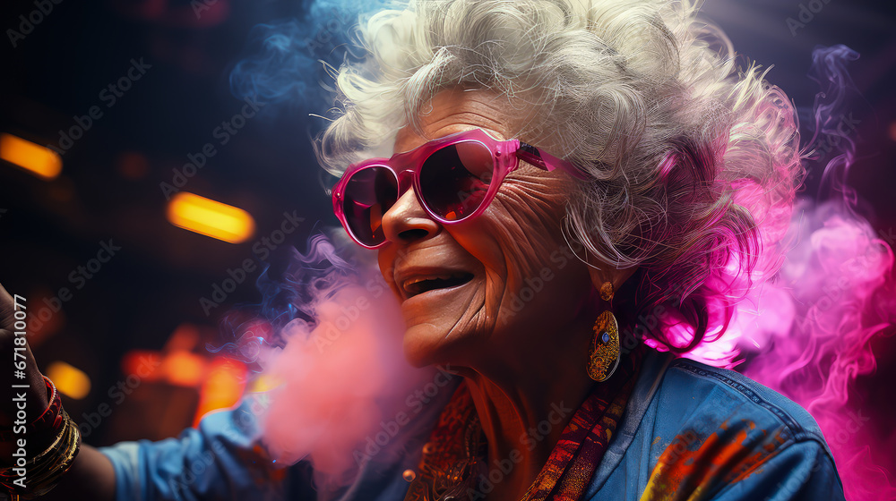 Stylish elderly woman in fashionable glasses dances funny in a nightclub. Senior woman having fun in neon lighting.