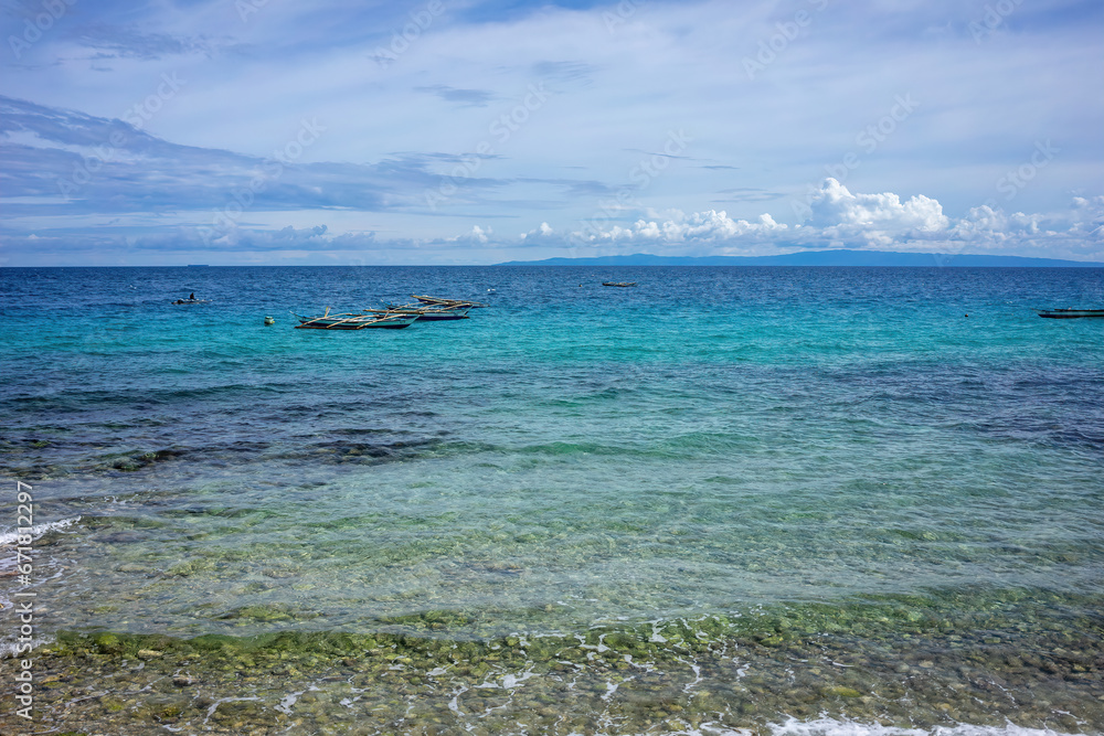 Crystal clear waters of a tropical beach with anchored boats. Gradient of blue hues from the shallow reefs to the deep ocean under a vast sky.