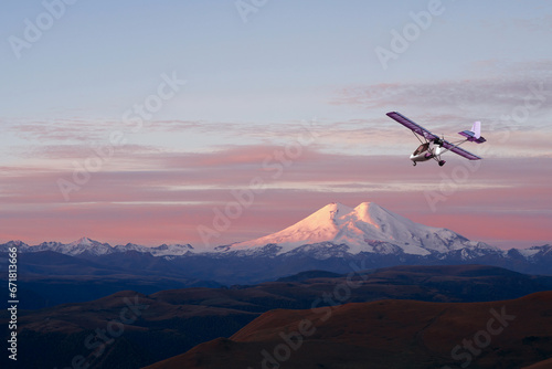 A picturesque panoramic view at dawn of a snow-capped volcano and a light two-seater plane in flight. Copy space.