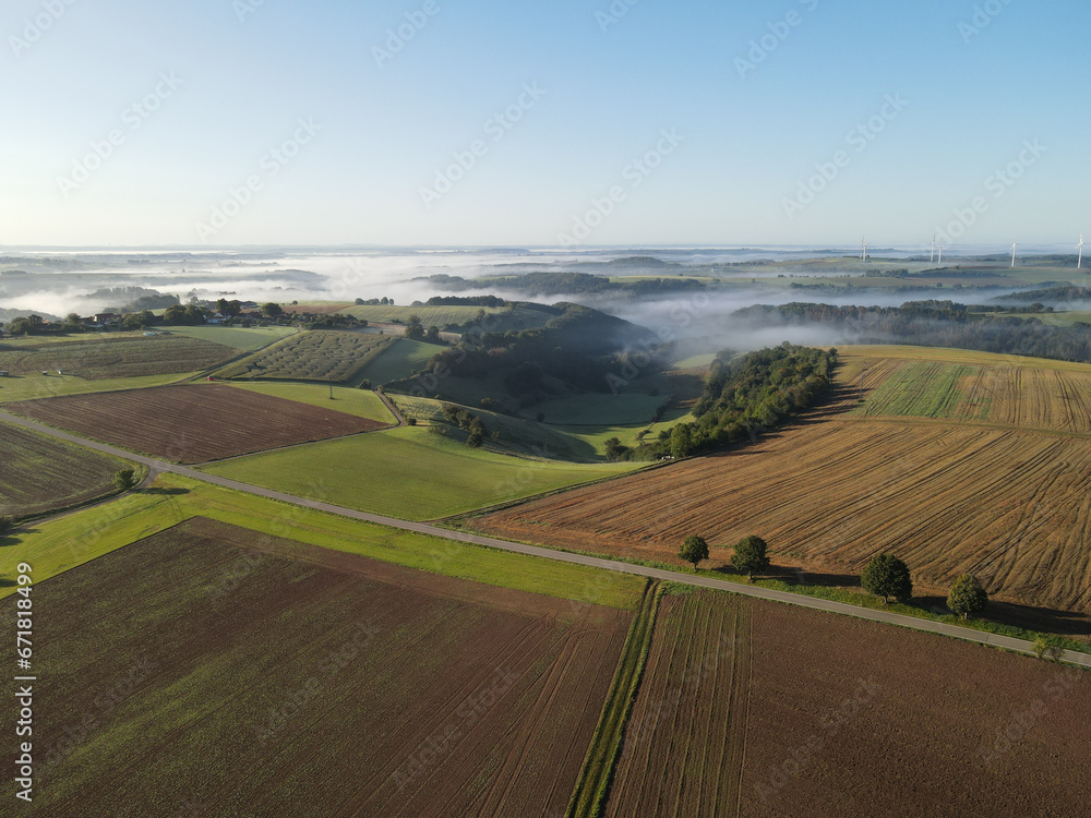 Aerial view of a landscape with fields and trees on a sunny and foggy morning