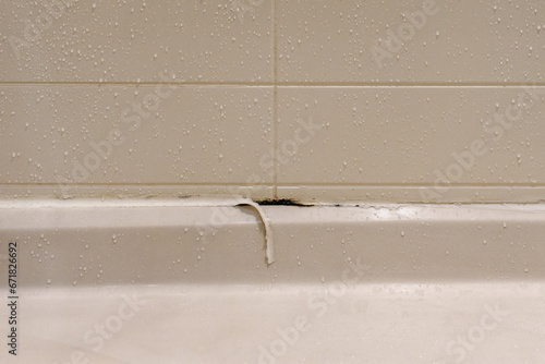 white shower stall with peeling caulking and mold growing underneath in a bathroom for unhealthy concept